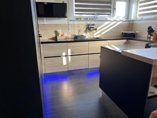 Moderne Küche mit hellen Holzfronten, dunklem Tisch und blauer LED-Beleuchtung.