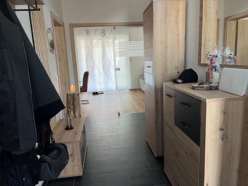 Heller Flur mit holzfarbenen Möbeln, Spiegel und sichtbarem Wohnbereich im Hintergrund.