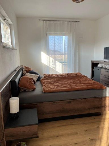 Gemütliches Schlafzimmer mit einem Bett, Holzmöbeln und großen Fenstern.